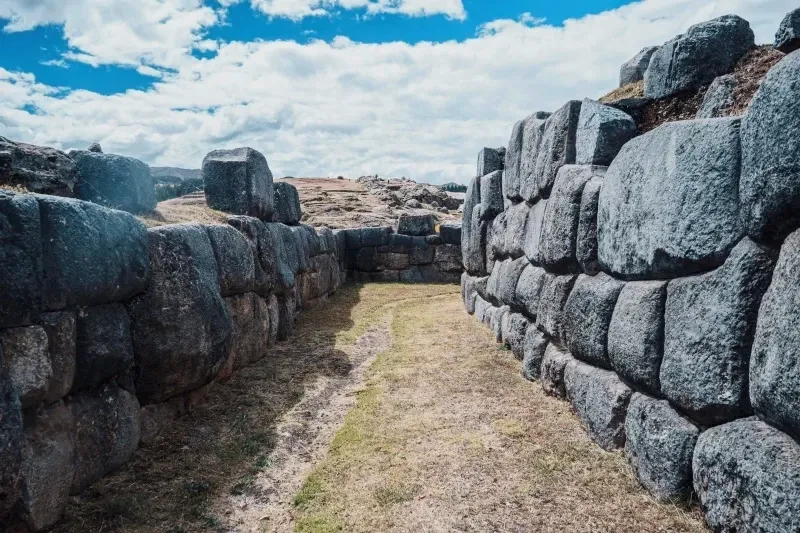 Precision of Inca Masonry and Engineering Intricate polygonal masonry of ancient Inca walls under a blue cloudy sky.
