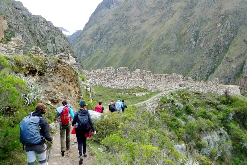 Hiking to Inca ruins in Peru A group of hikers with backpacks walking along a mountain path toward ancient Inca stone ruins.