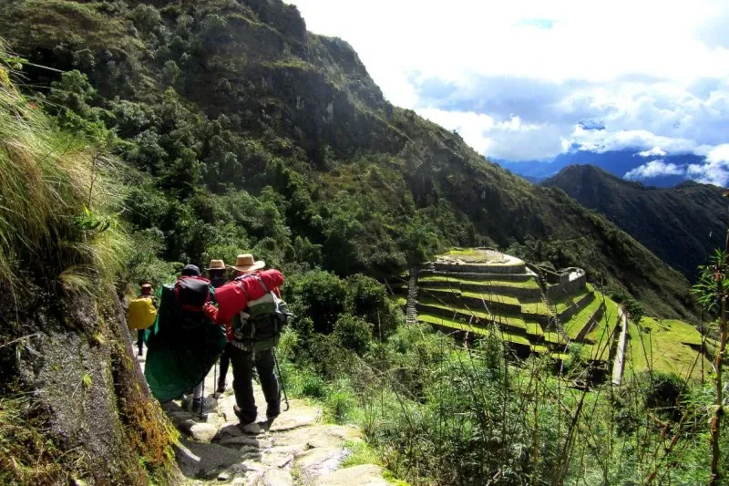 Hiking the Majestic Inca Trail A group of hikers with backpacks walking down an ancient stone path toward Inca agricultural terraces and ruins.