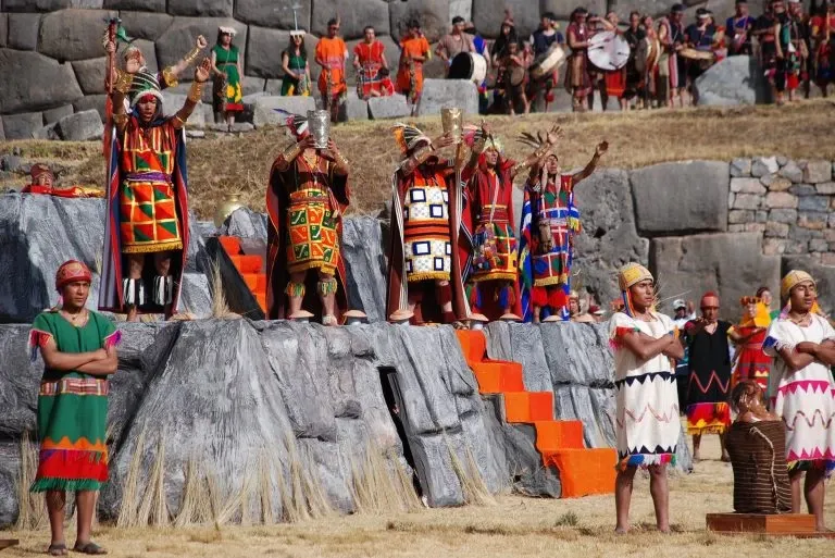 Incan priests in colorful ceremonial attire performing a traditional offering ritual with golden vessels at Sacsayhuaman.