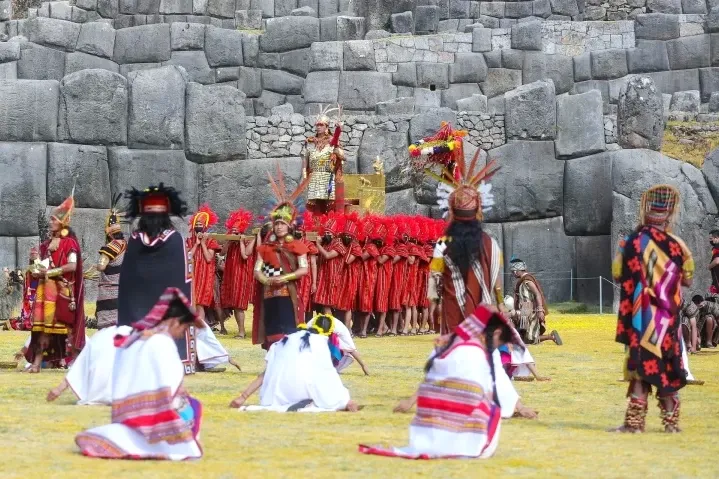 Large procession of Incan participants in red and gold outfits at the Sacsayhuaman archaeological site in Cusco.