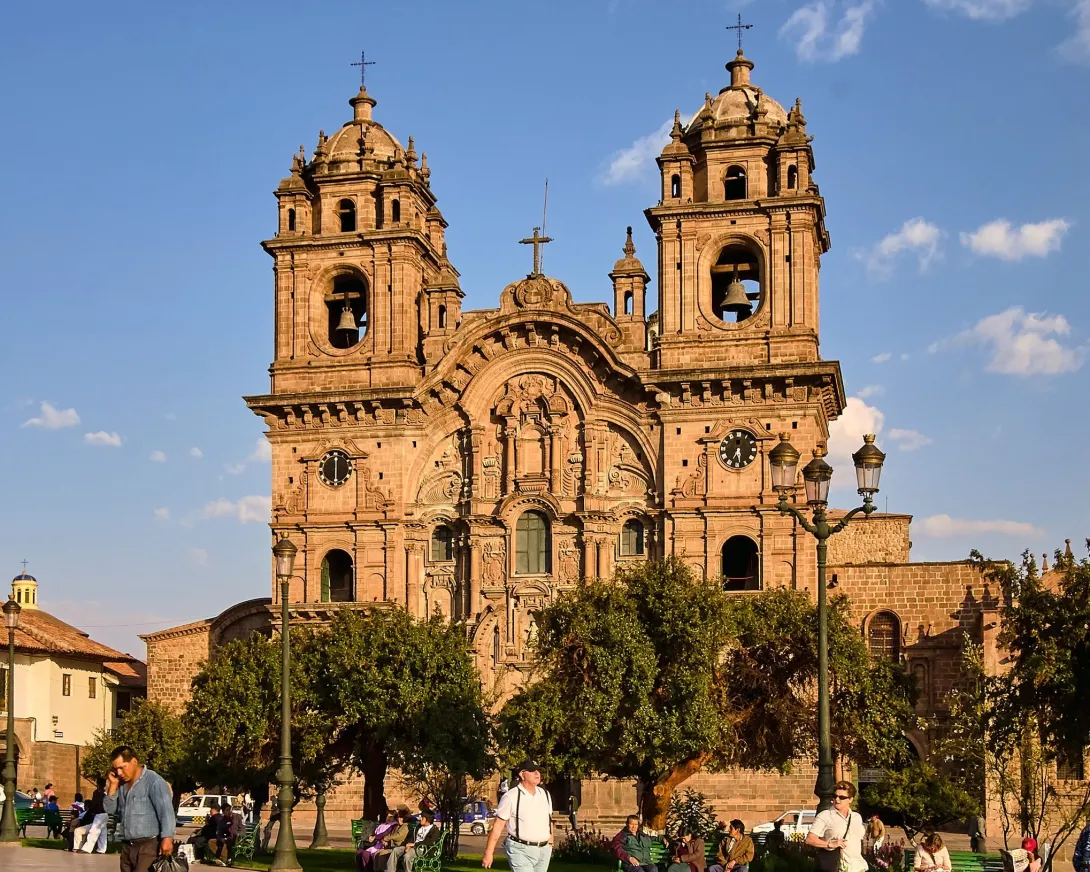 The golden stone facade of the Company of Jesus Church during sunset in the Main Square of Cusco.