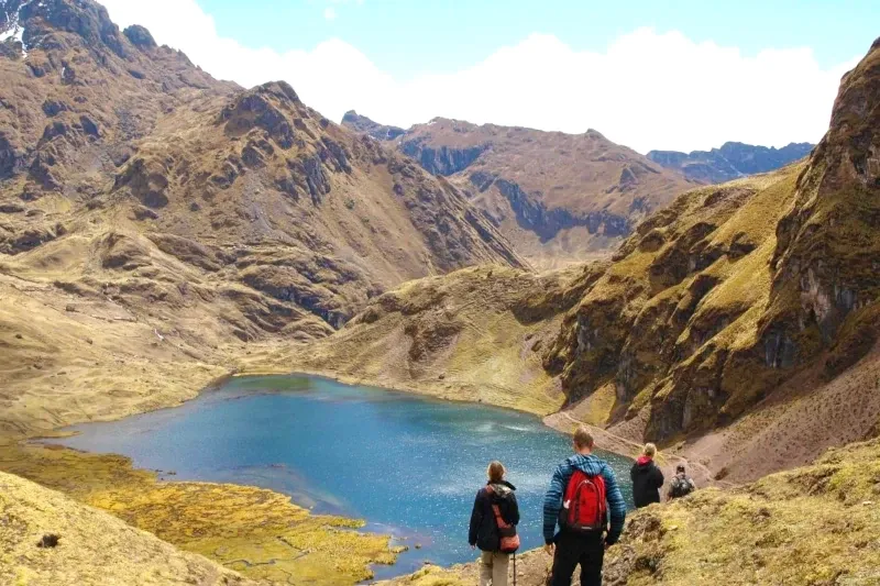 A group of hikers looking down at a bright blue alpine lake surrounded by steep mountains in the Lares Valley.