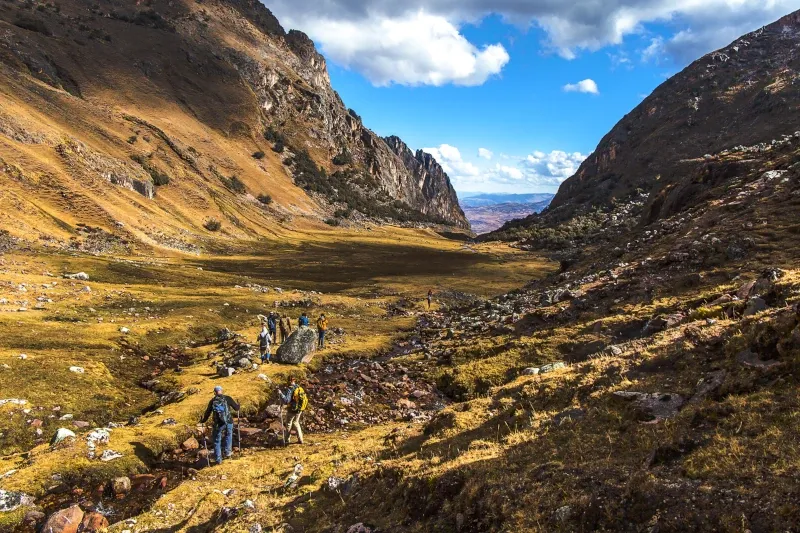 Hikers walking through a vast, golden mountain valley under a blue sky during a Lares valley tour.