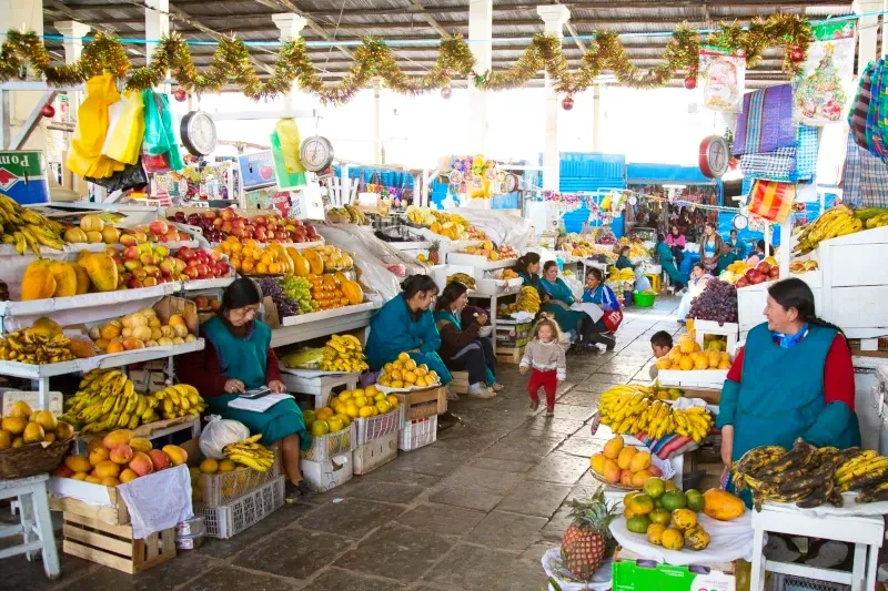 Local Andean women in traditional aprons arranging fruit displays inside the San Pedro Market.
