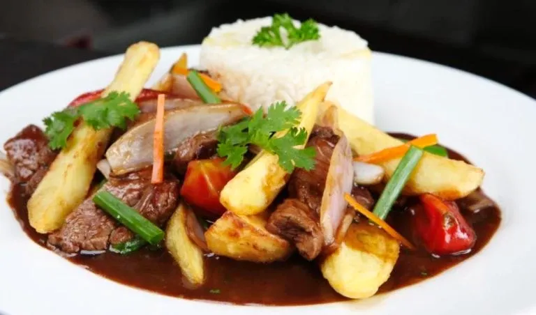 A delicious plate of Lomo Saltado, a traditional Peruvian beef stir-fry with onions, tomatoes, and crispy fries served with white rice.