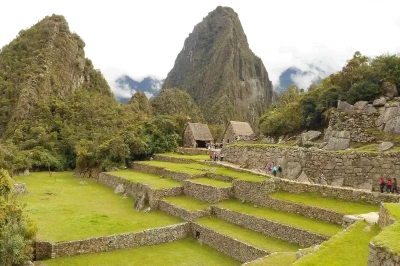 Lush green agricultural terraces and traditional stone houses with the Huayna Picchu mountain towering behind.