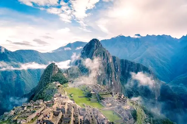 The lost city of Machu Picchu surrounded by lush green mountains and white clouds.