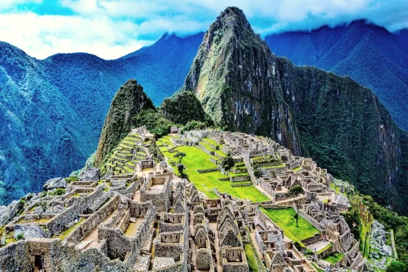 Panoramic aerial view of the ancient Inca citadel of Machu Picchu with Huayna Picchu mountain in the background under a blue sky.