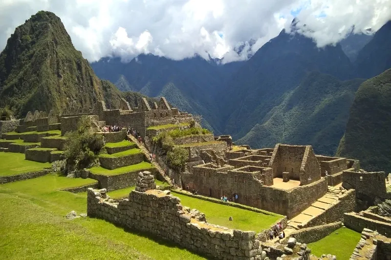 Panoramic view of the Machu Picchu citadel with the iconic Huayna Picchu mountain in the background under cloudy skies.