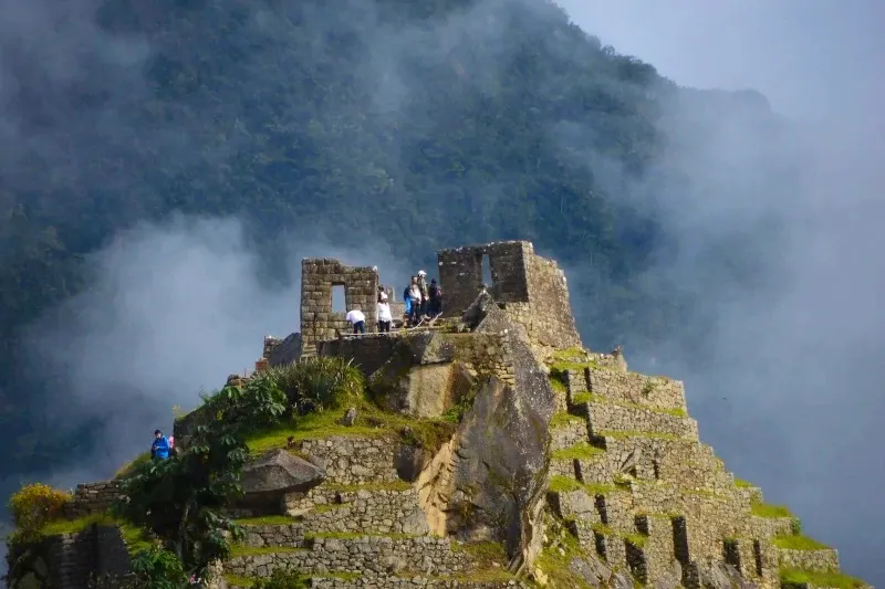 Stone Inca structure on a mountain peak surrounded by mystical clouds and lush green vegetation.