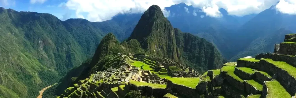 Panoramic view of the ancient Inca citadel of Machu Picchu with Huayna Picchu mountain in the background under a blue sky.