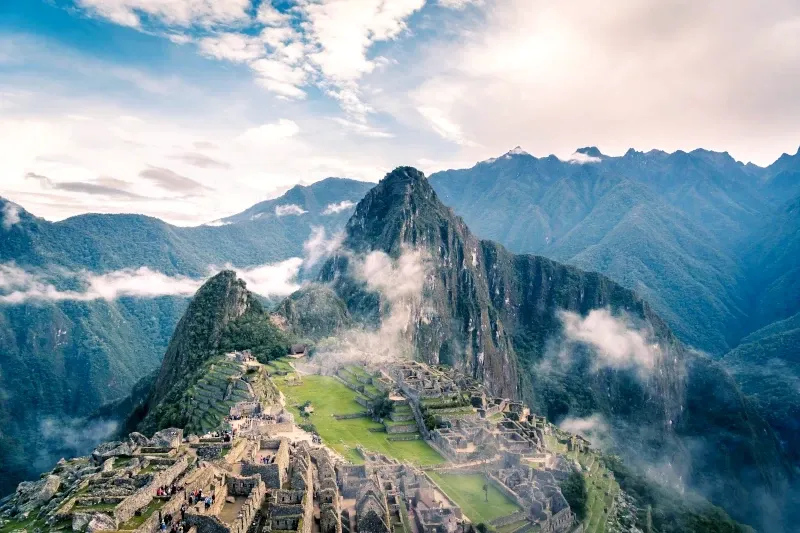 Iconic view of the Machu Picchu Inca citadel with Huayna Picchu mountain in the background under a blue sky.