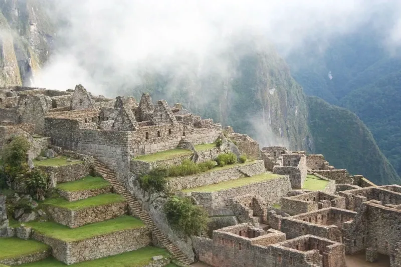 Detailed view of the stone structures and terraces of the Machu Picchu citadel with misty mountains in the background.