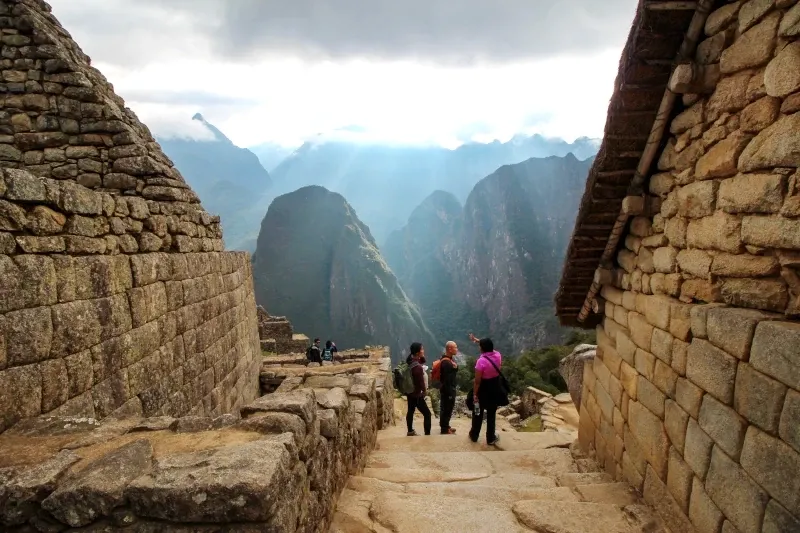 Guided tour at Machu Picchu ruins A tour guide showing tourists the ancient stone structures of the Machu Picchu citadel with Huayna Picchu mountain in the background.