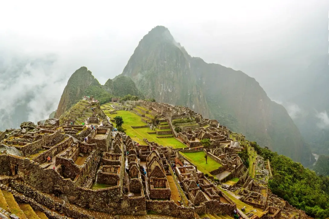 Wide shot of the stone terraces and urban sector of Machu Picchu on a misty day.