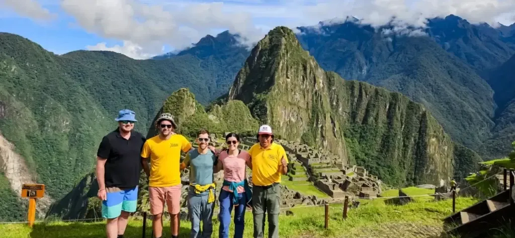A diverse group of travelers posing with their professional tour guides wearing yellow Xtreme Tourbulencia shirts at the Machu Picchu citadel.