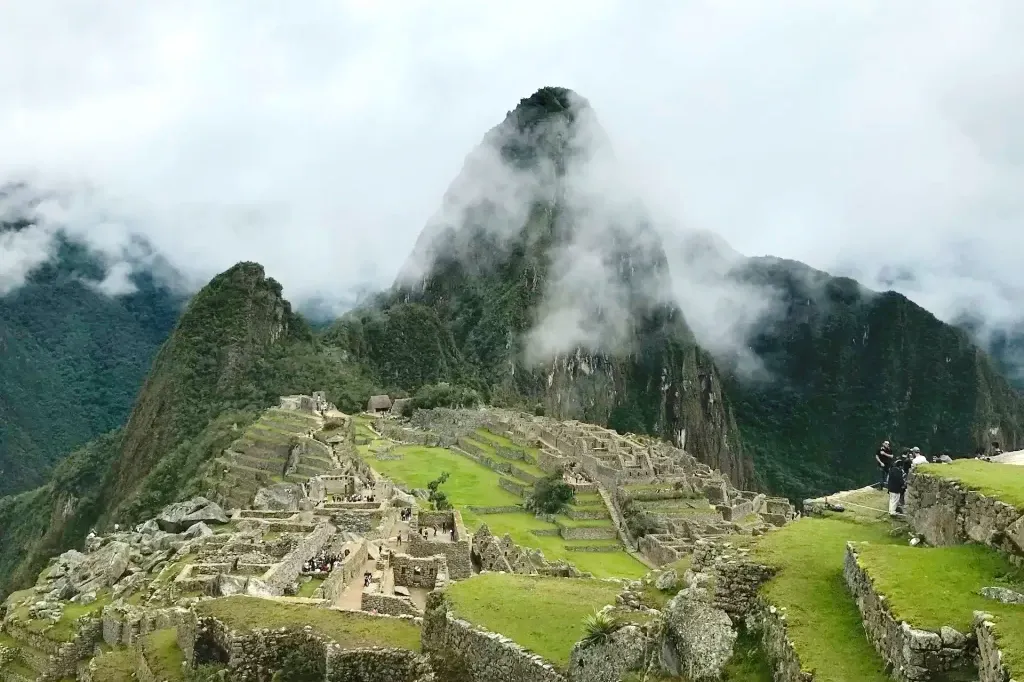 The ancient Incan city of Machu Picchu surrounded by lush green mountains and white clouds clinging to the peaks.