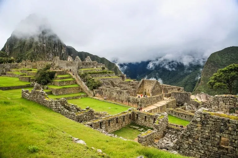The ancient ruins of Machu Picchu surrounded by misty clouds and lush green Andean mountains.