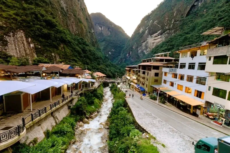 High-angle view of the main road and river in Aguas Calientes nestled between towering Andean mountains.