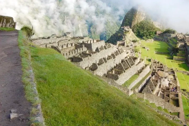 Stone buildings and terraces of Machu Picchu partially covered by mist and clouds in the morning.