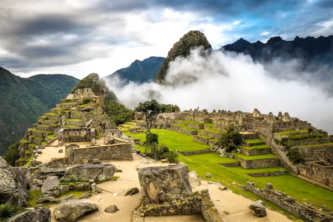 Machu Picchu ruins under a cloudy sky Scenic view of the Machu Picchu archaeological site with clouds rolling over the surrounding green mountains.