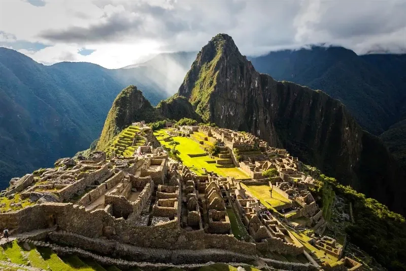 Sun rays shining over the stone ruins and agricultural terraces of the Machu Picchu citadel.
