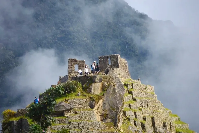 Travelers exploring the upper sacred section of Machu Picchu surrounded by mystical mountain clouds.