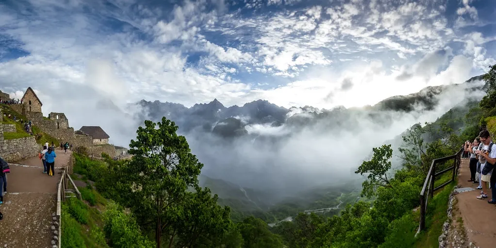 Panoramic view of the Machu Picchu citadel with low clouds swirling around the Huayna Picchu mountain and ancient stone structures.