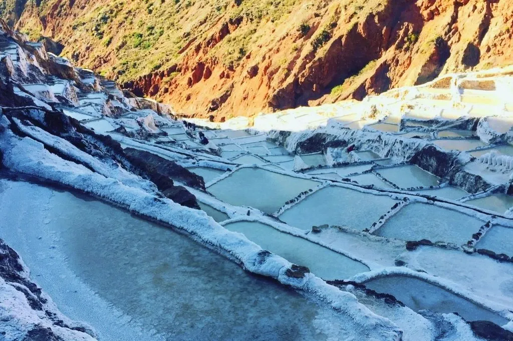 Terraced salt ponds reflecting the sunlight against the reddish mountain slopes of the Sacred Valley of the Incas.