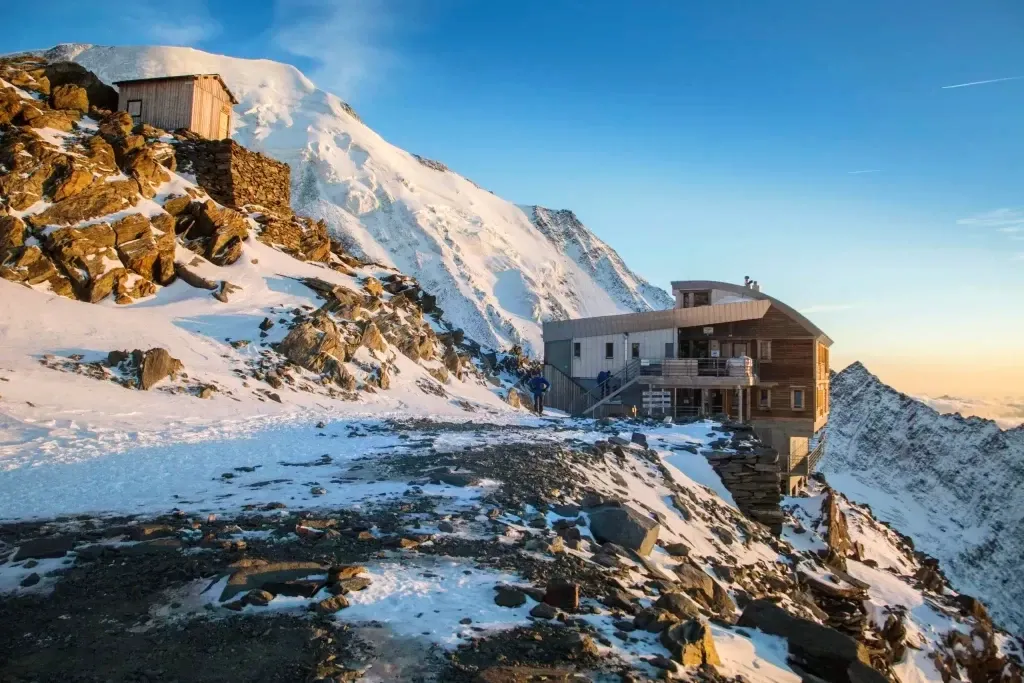 A modern mountain hut built on a rocky cliff surrounded by snow on the Mont Blanc massif in the Alps.
