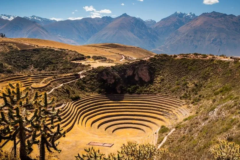 Overhead view of the circular agricultural terraces of Moray with the snow-capped Andes in the distance.
