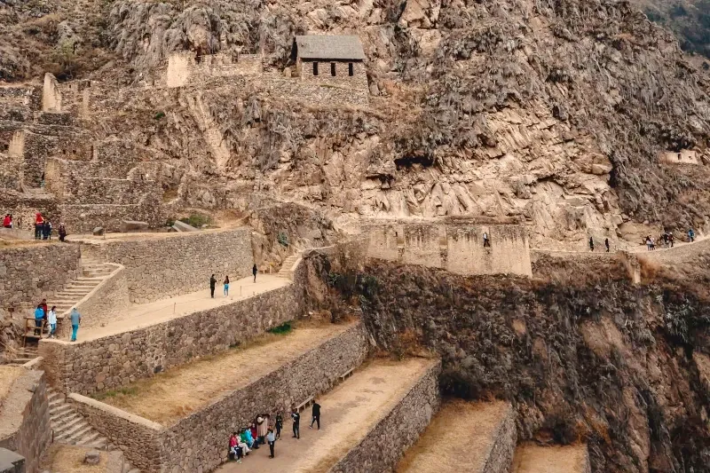 Panoramic view of the massive Inca agricultural terraces and stone structures at the Ollantaytambo fortress with tourists.