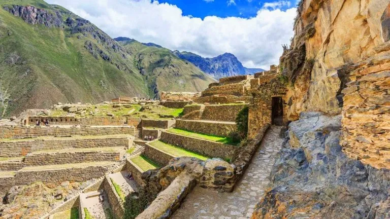 Stone stairs and ancient walls of the Ollantaytambo fortress with a view of the surrounding Sacred Valley mountains.