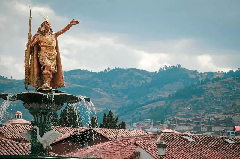 Golden statue of Inca Emperor Pachacutec on a fountain with the city of Cusco in the background.