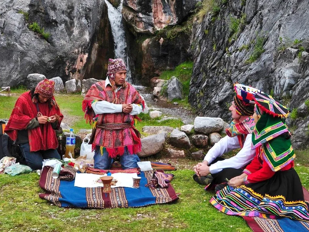 An Andean priest performing a "Pago a la Tierra" (Offering to Mother Earth) ceremony near a waterfall in Cusco with travelers.
