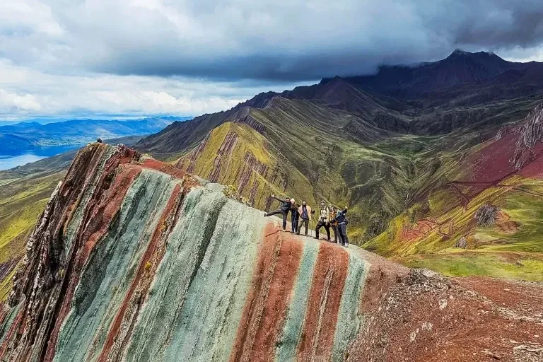 A group of hikers celebrating on the sharp, colorful ridges of Pallay Punchu mountain overlooking a lake.