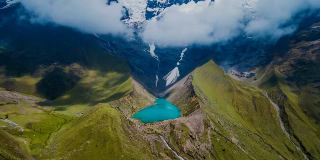 Panoramic view of the turquoise Humantay Lake nestled between green mountain ridges and a white glacier.