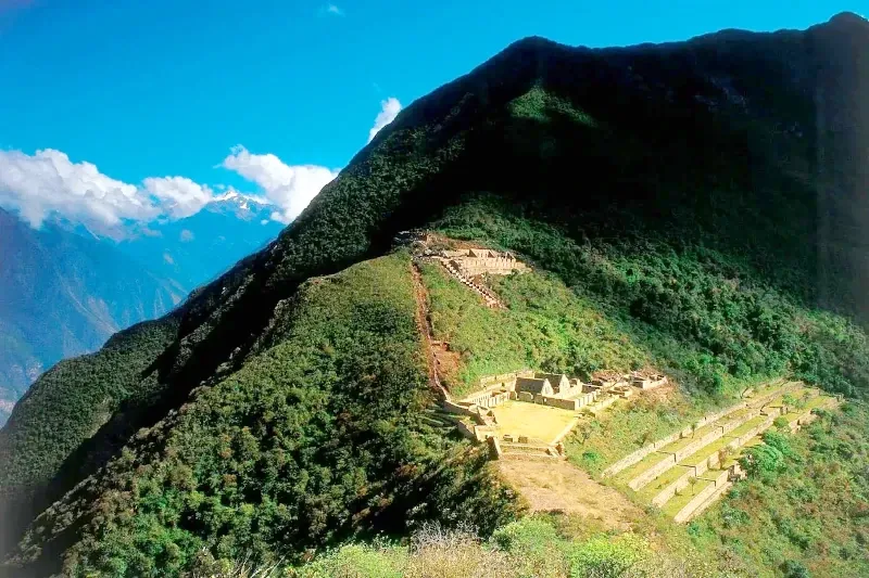 Choquequirao ruins mountain view Aerial panoramic view of the Choquequirao ruins nestled on a green mountain ridge under a blue sky.