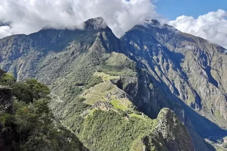 High angle panoramic view of the Machu Picchu Inca citadel surrounded by lush green mountains and clouds.