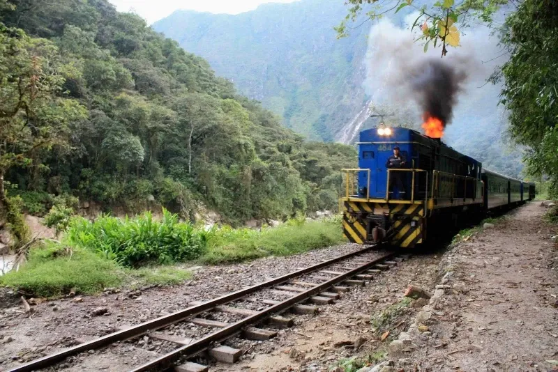 A blue PeruRail locomotive releasing smoke while traveling along the tracks in the high Andes.