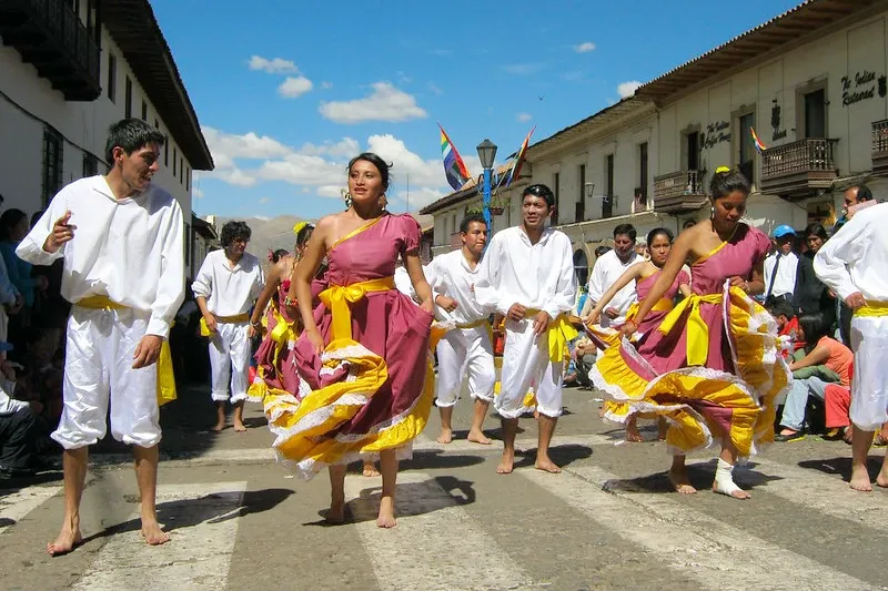Group of young dancers in traditional white and purple costumes performing a coastal dance on a city street.