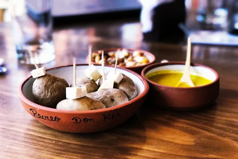 Small native Peruvian potatoes served in a traditional clay bowl with cheese cubes on toothpicks and a yellow dipping sauce.