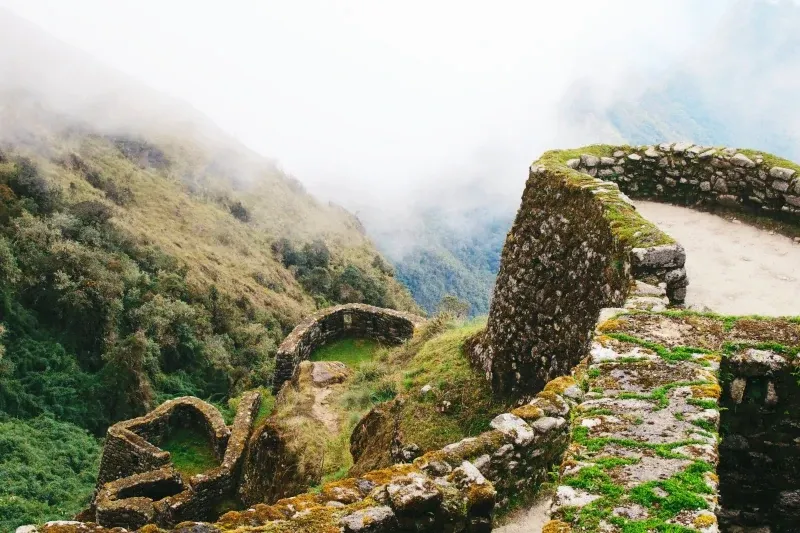 The stone structures of Phuyupatamarca perched on a mountain ridge, surrounded by mist and the Andean cloud forest.