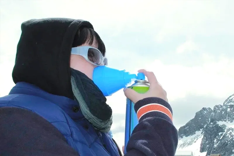 Close-up of a traveler using a blue portable oxygen mask and canister to cope with high altitude in the mountains.
