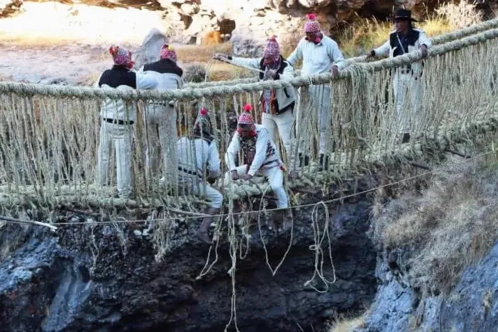 Local communities in traditional clothing weaving the Qeswachaka grass bridge in Cusco
