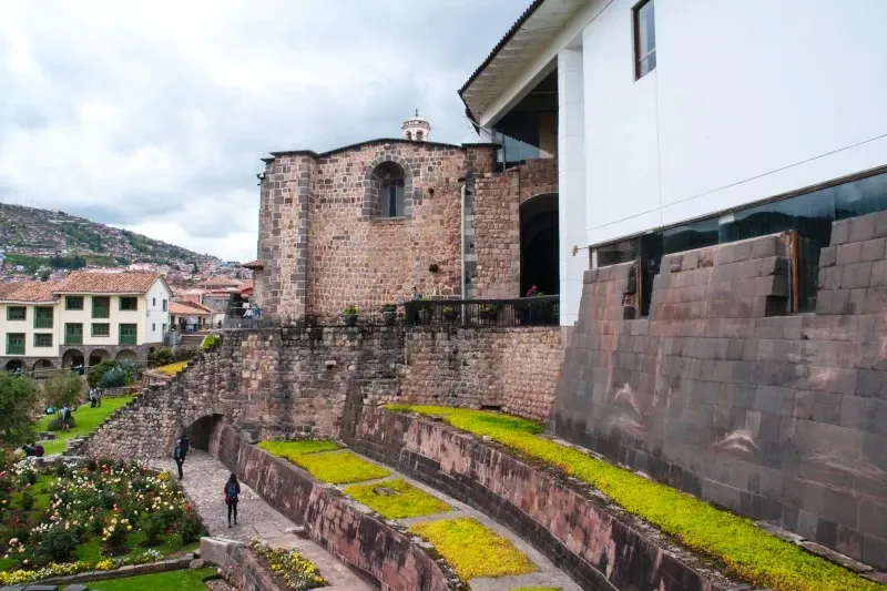 The ancient Inca walls of Qorikancha Temple with gardens and colonial architecture in Cusco.