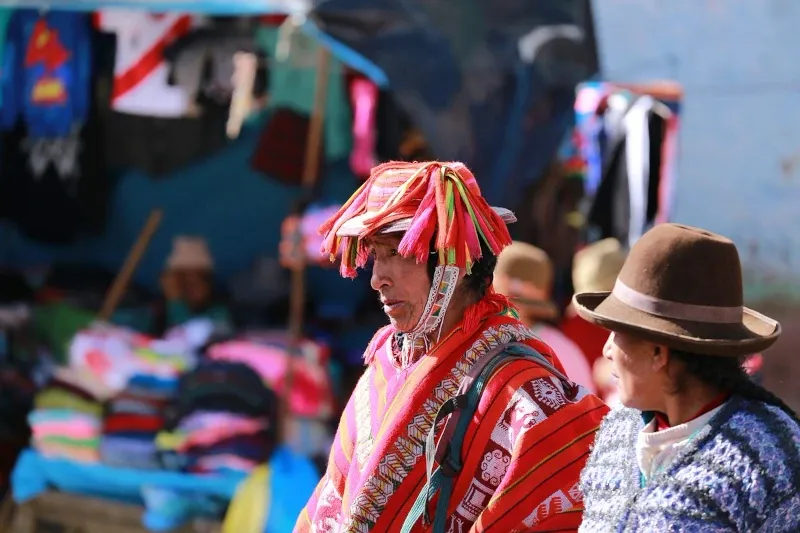 Authentic Quechua Traditions A Quechua woman wearing a traditional decorated hat and vibrant red poncho at a local market in the Sacred Valley.