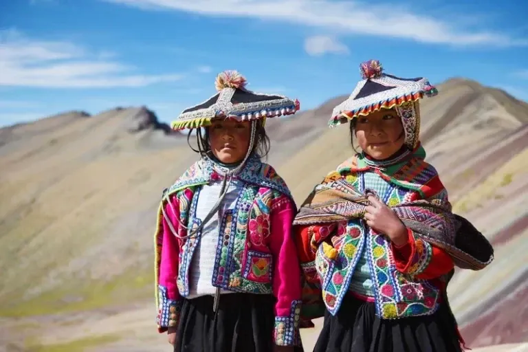 Two young girls in traditional colorful Andean outfits standing at the Rainbow Mountain (Vinicunca) in Cusco.