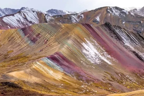 The colorful mineral layers of Vinicunca Rainbow Mountain with snow-capped peaks in the background.